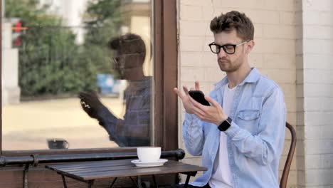 Young-Man-Using-Smartphone-and-Laptop-in-Outdoor-Cafe