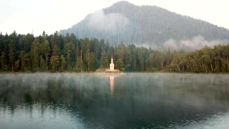 Drone-volador-rápido-por-encima-de-la-iglesia-de-lanzamiento,-bosque-de-otoño-en-la-isla-dentro-del-lago-en-el-tiempo-soleado