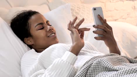 Junge-afrikanische-Frau-mit-Smartphone-beim-Liegen-im-Bett