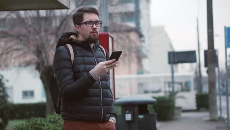 Man-is-scrolling-screen-of-mobile-phone-on-bus-station