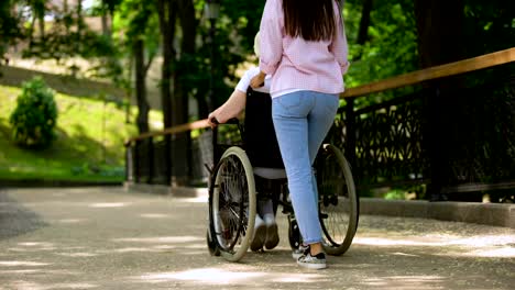 Mujer-que-ayuda-a-la-vieja-paciente-discapacitada-pasar-tiempo-en-el-jardín-del-hospital,-medicina