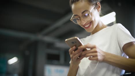 young-smiling-stylish-beautiful-woman-in-white-t-shirt-and-transparent-eyewear-is-using-smartphone-outdoors.-woman-searching-something,-scroling-social-networks,-chating-and-texting