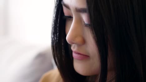 Close-up-smile-young-Asian-woman-using-mobile-phone-browsing-social-media-communication-and-shopping-online-while-sitting-on-the-sofa-at-home.