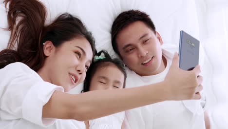 Asiatische-Familie-liegen-über-das-Bett-spielen-und-suchen-Anwendung-Smartphone,-während-im-Schlafzimmer-liegen