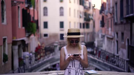 Positive-weibliche-Bloggerin-in-stilvolle-Sonnenbrille-tippen-Text-für-SMS-Nachricht-mit-Informationen-über-Venedig-Stadt