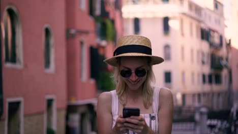 Slow-motion-effect-of-cheerful-hipster-girl-in-stylish-sunglasses-typing-text-message-for-sending-to-friend-during-leisure-time-on-Venice-urban-setting