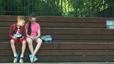 The-older-sister-and-brother-are-sitting-on-the-street,-looking-at-smartphones.