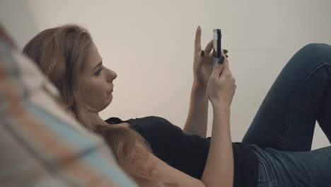 Beautiful-girl-with-a-mobile-phone-resting-on-a-sofa-at-home.-Blonde-girl-with-a-mobile-phone-in-her-hands.