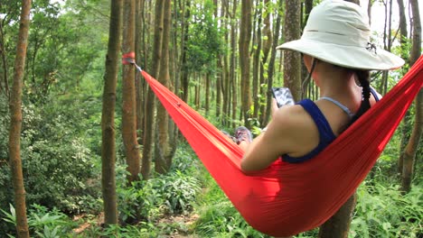 Mujer-relajándose-en-hamaca-con-teléfono-inteligente-en-la-selva-tropical,4k