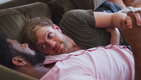 Loving-Male-Gay-Couple-Relaxing-Lying-On-Sofa-At-Home-Hugging-And-Kissingæ