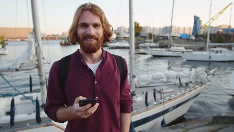 Lächelnder-Mann-mit-Smartphone-in-der-Nähe-von-River