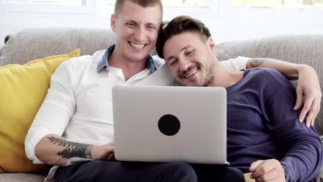 Gay-couple-relaxing-on-couch-using-laptop-computer.-Looking-at-screen.