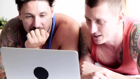 Gay-couple-in-bed-using-laptop-computer.-Browsing-around.