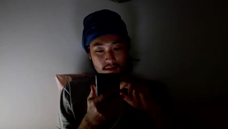 Attractive-Asian-man-using-a-mobile-phone-while-Lying-on-Bed-at-home-Late-at-Night.-Browsing-social-media-and-watching-a-video.