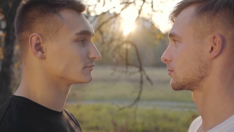 Close-up-faces-of-two-Caucasian-men-looking-at-each-other-in-sunlight.-Serious-adult-boys-standing-outdoors.