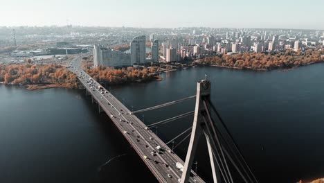 Unglaubliche-Drohnenansicht-von-Kiew-mit-Hochhäusern-und-Bauten-im-Hintergrund.-Drohne-fliegt-über-Autobrücke-über-breiten-Fluss-in-Großstadt