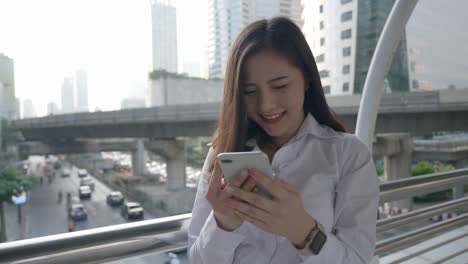 Excited-business-asian-woman-celebrating-good-news-checking-smart-phone-in-the-modern-city-center-in-the-evening-of-Bangkok-Thailand.-Concept-Technology-communication,-success-by-mobile-phone