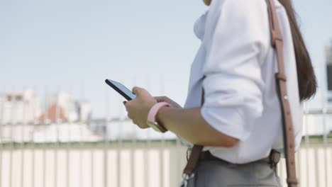 Close-up-Asian-businesswoman-in-a-white-shirt-is-using-a-smartphone-texting-sharing-messages-on-social-media-while-outside-the-morning-at-a-public-park.