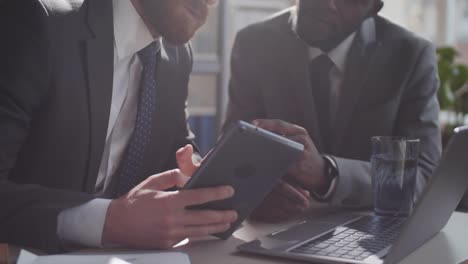 Zwei-verschiedene-männliche-Kollegen,-die-Tablet-verwenden-und-am-Office-Desk-sprechen