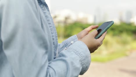 Close-up-hand-asian-teenage-girl-using-smartphone-browsing-social-media-and-shopping-online-while-standing-outdoors-at-a-public-park-on-the-beautiful-sunset.