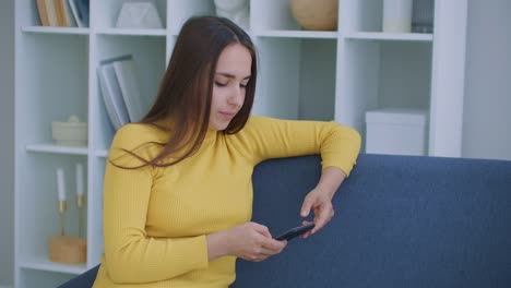 Mujer-escribe-mensajes-usando-el-teléfono-móvil-sentado-en-el-sofá-en-la-sala-de-estar