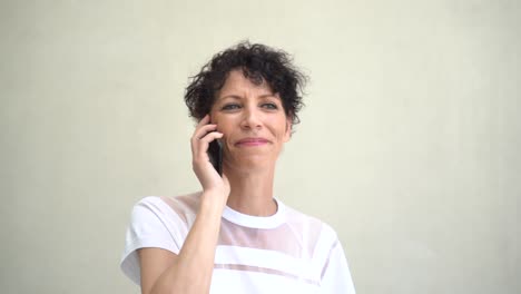 Close-up-shot-of-Caucasian-mature-woman-talking-on-mobile-phone-against-wall