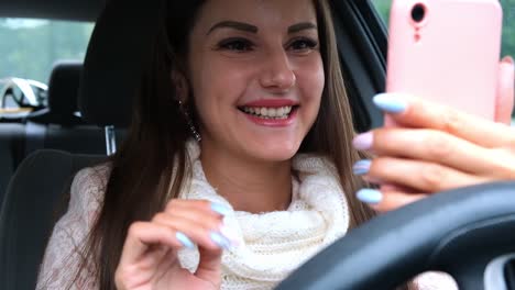 Mujer-alegre-usando-un-teléfono-inteligente-en-un-coche-de-conducción.-Retrato-de-una-mujer-alegre-mirando-el-teléfono-mientras-conduce