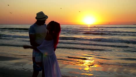 Couple-of-young-man-and-woman-meeting-on-a-sandy-beach-and-kissing-with-passion-at-sunrise