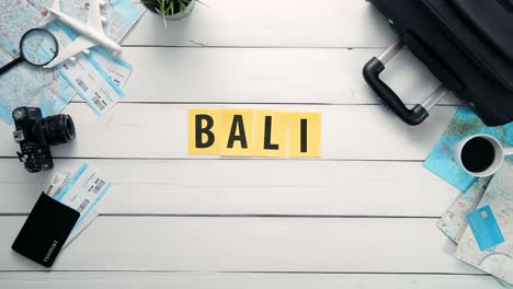 Lapso-de-tiempo-de-la-vista-superior-de-las-manos-puesta-en-la-palabra-escritorio-blanco-"BALI"-decorada-con-artículos-de-viaje