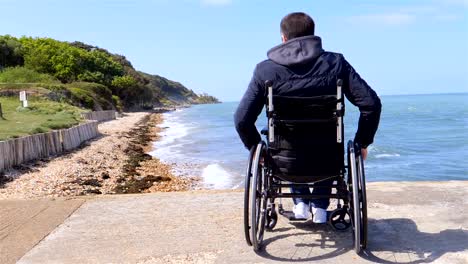 La-parte-trasera-del-hombre-discapacitado-en-silla-de-ruedas-en-la-playa