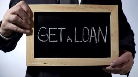 Get-a-loan-written-on-blackboard,-businessman-holding-sign,-business-concept