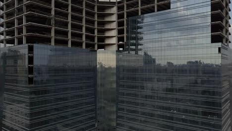 Rascacielos-con-una-fachada-de-cristal-cerca-del-viejo-edificio-de-multi-apartamento.-La-cámara-se-mueve-desde-el-edificio-nuevo-a-la-vieja-casa.-Vista-aérea