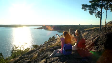 Happy-Female-Couple-Drinking-Champagne-on-a-High-Rock-in-the-Sunshine