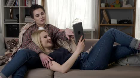 Lesbian-couple-is-resting-on-the-couch,-using-tablet-computer,-speaking,-family-idyll,-lgbt-60-fps