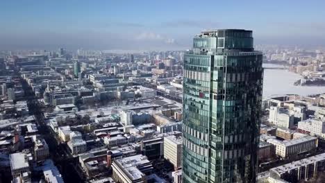 Aerial-view-of-skyscraper-is-in-the-middle-of-the-city-in-winter,-blue-sky-sky-and-snowy-roofs-of-buildings-background