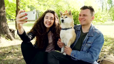 Proud-dog-owners-happy-couple-are-taking-selfie-with-beautiful-pet-having-fun-and-fussing-it-looking-at-smartphone.-Modern-lifestyle,-animals-and-technology-concept.