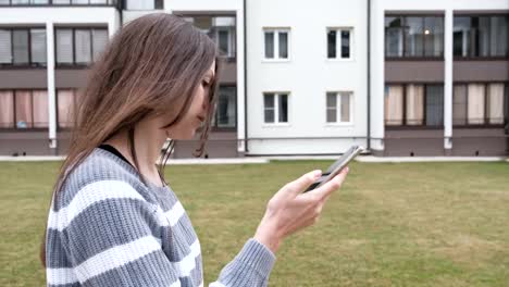 Beautiful-brunette-woman-reading-a-message-on-mobile-phone-walking-near-the-home.