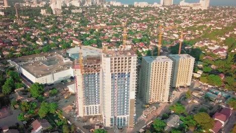 Aerial-drone-shot.-Construction-of-high-rise-buildings-in-the-developing-area-of-a-large-city.-Sunset-shot.-Inscriptions-floors,-building-cranes-and-many-houses-under-construction.-wide-shot