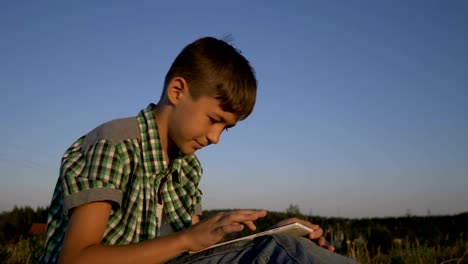 tableta-de-uso-muchacho-sentado-en-el-campo-al-atardecer,-al-aire-libre