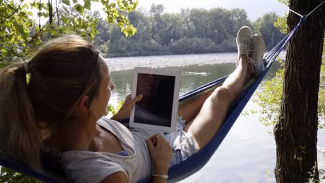 Young-woman-using-digital-tablet-on-hammock