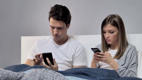 Joven-pareja-utilizando-Smartphone-mientras-relajante-en-la-cama