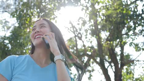 Hermosa-asiática-joven-con-smartphone-en-el-parque.-Mujer-con-smartphone-de-árbol-un-natural-en-el-fondo.