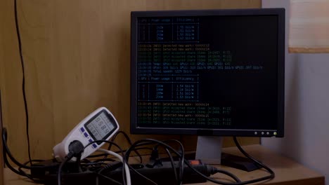 Leistungsmesser-zeigt-den-Stromverbrauch-des-Astraleums-Kryptowährung-Bergbau-Rig-mit-Mining-Prozess-anzeigen-auf-Monitor-an-Computer-angeschlossen.