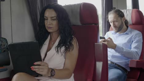 Business-man-and-woman-commuting-to-work-using-tablet-and-smartphone-surfing-on-internet-technology-and-train-travel-with-train-concept