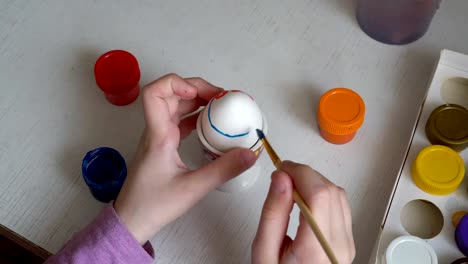 A-little-girl-draws-on-a-white-Easter-egg-with-paints-and-a-brush.-Close-up.-The-view-from-the-top.-4K.