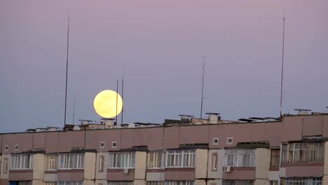 Großer-Vollmond-über-dem-Dach-eines-mehrstöckigen-Gebäudes-bewegt-sich-nach-oben