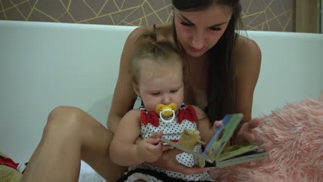 Mother-and-Her-Cute-Daughter-are-Sitting-On-a-Couch-in-the-Living-Room.-They're-Reading-Children's-Book