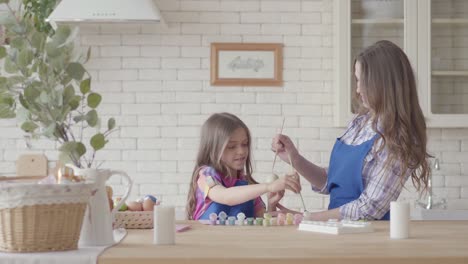 Niña-pequeña-pintando-huevos-con-su-madre-usando-un-cepillo-pequeño.