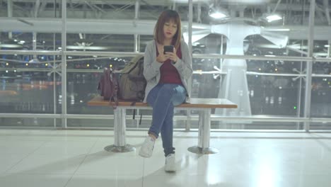 Asiatische-Frau-mit-Smartphone,-während-sie-auf-dem-internationalen-Flughafen-sitzt.