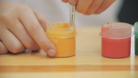 Creative-boy-is-mixing-and-stirring-yellow-paint-in-a-jar-with-a-help-of-nude-paint-brush.